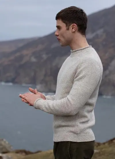 side angle shot of man wearing cream knit sweater with Irish landscape in background