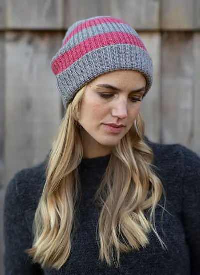 woman with long blonde hair looking down and wearing a grey and pink stripe wool knit beanie hat