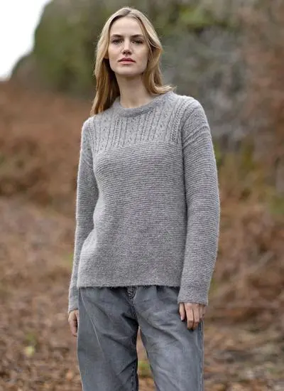 blonde woman standing in rocky outdoor area wearing a grey eyelet knit sweater 