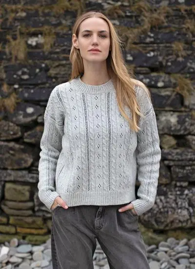 blonde woman wearing off-white eyelet cable crew sweater against stone wall 