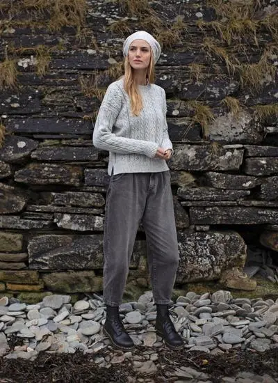 full body shot of blonde woman standing in rocky outdoor area wearing a grey eyelet knit sweater
