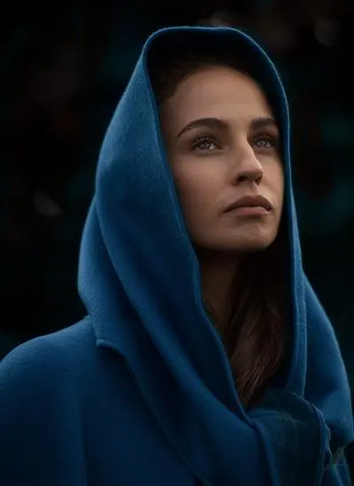 Close up shot of woman outside wearing blue cape with hood.
