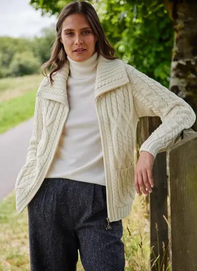 brown haired woman in park leaning against wooden fence wearing open cream aran zip cardigan