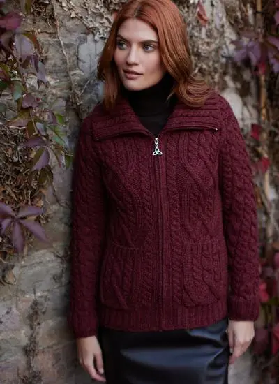 red haired woman standing near wall with red vines wearing deep red aran zip cardigan 