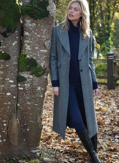 Blonde woman in woodland area wearing longline blue herringbone tweed coat with buttons open