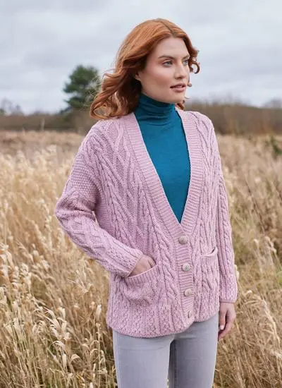 Red hair lady wearing a pink aran cardigan, with a blue polo neck under it, in a field with her hand in her pocket