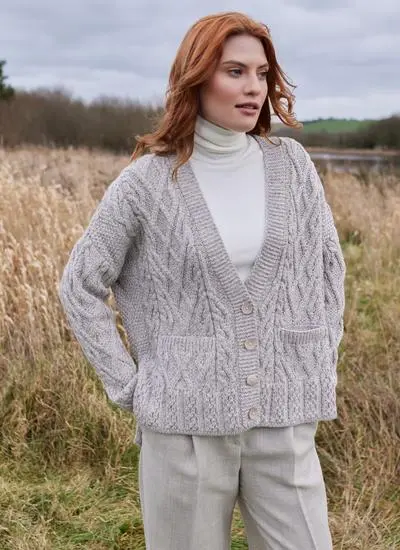 red haired woman standing in field of reeds wearing a grey aran cardigan with white polo beck underneath