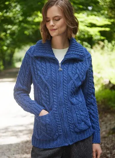 woman with short brown hair standing in forest wearing a blue zip aran cardigan with one hand in pocket