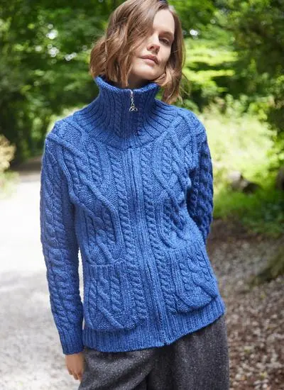 woman with short brown hair standing in forest wearing a blue zip aran cardigan with high collar