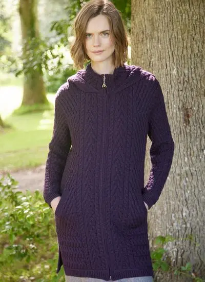 woman with short brown hair in wooded area wearing purple aran coatigan with hands in pockets