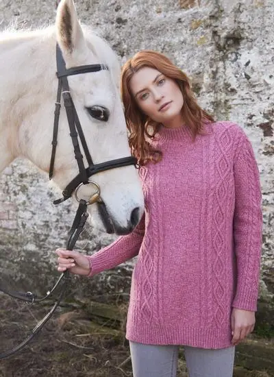red haired woman wearing pink turtle neck sweater in stables with white horse